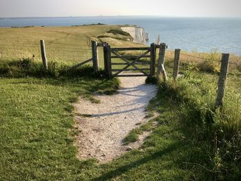 Wooden fence on field by sea against sky
