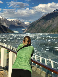 Rear view of woman looking at mountain by frozen lake against sky