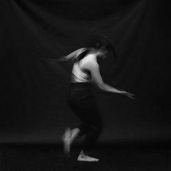 Side view of woman dancing against black background