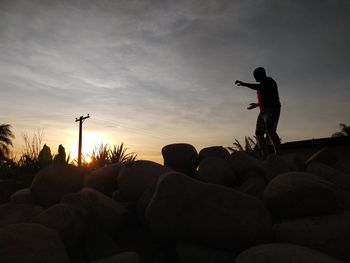 Silhouette people standing on rock against sky during sunset