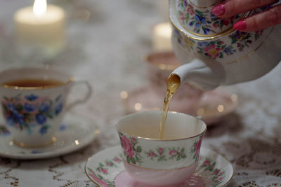 Cropped hand of woman pouring tea on table at home