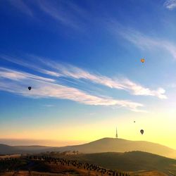 Hot air balloons flying over landscape against sky during sunset