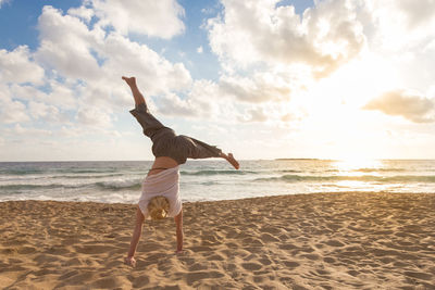 Full length of woman with performing handstand on beach against sky