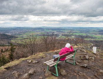 Rear view of woman sitting on bench against sky