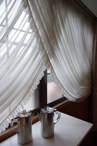 Close-up of jugs on table by window