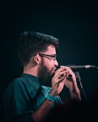 Portrait of young man holding eyeglasses against black background