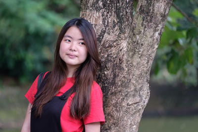 Portrait of smiling young woman standing against tree trunk