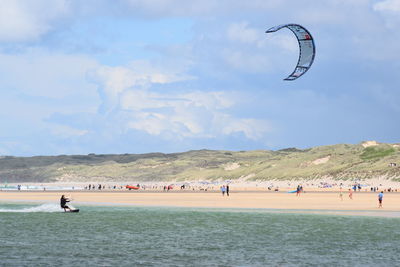 People enjoying kitesurfing with beach against sky