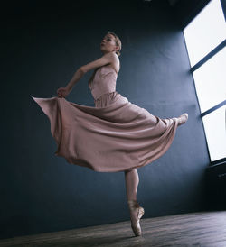 A ballerina in a pink dress and punts moves around the room with a fluttering dress