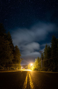 Road amidst trees against sky at night