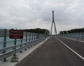 Road sign by bridge against sky