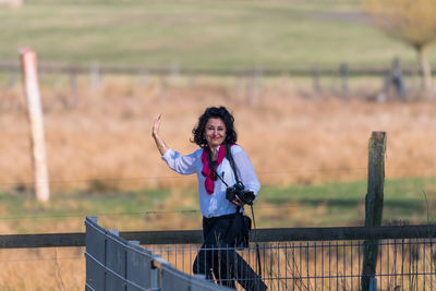 Portrait of smiling woman waving hand while walking on field