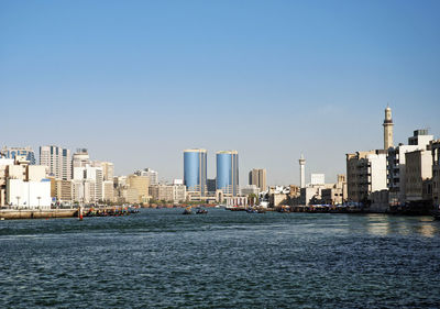 Sea by city buildings against clear sky