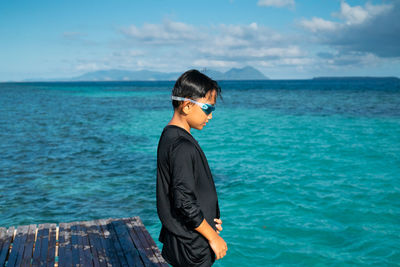 Side view of boy standing on pier over sea against sky