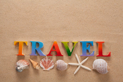 Directly above shot of travel text with seashells on sand at beach