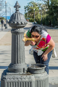 Thirsty woman drinking clean water in an old metal drinking fountain in the city of barcelona