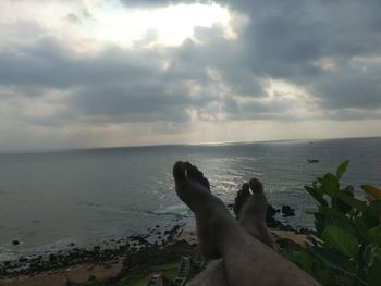 Low section of woman relaxing on beach against sky