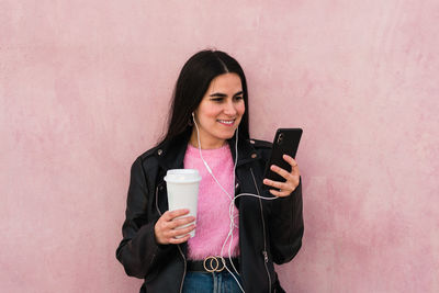 Young woman listen music and looks her smartphone in a pink background