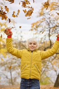 Smiling young woman throwing autumn leaves