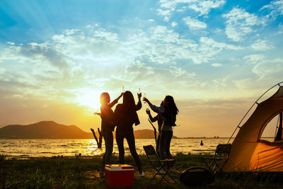 Silhouette people on beach against sky during sunset