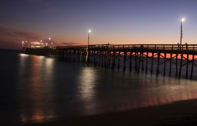 Illuminated pier on sea against sky at dusk