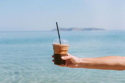 Cropped hand holding coffee against sea