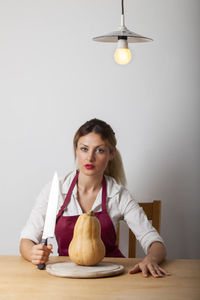Portrait of young woman holding ice cream on table against wall
