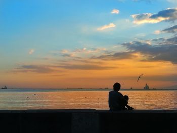 Silhouette man sitting by sea against sky during sunset