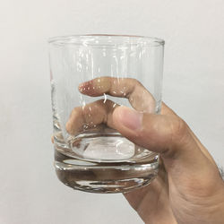 Close-up of hand holding glass over water against white background