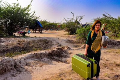 Portrait of smiling woman with suitcase standing on land