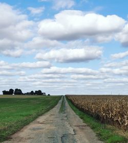 Dirt road amidst field against sky