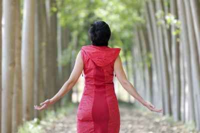 Rear view of woman with arms outstretched standing amidst trees