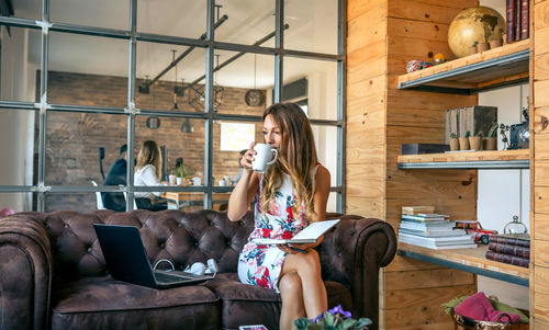 Young woman drinking coffee while sitting on sofa in office