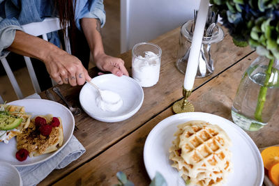 Midsection of woman spreading yogurt on plate at wooden table