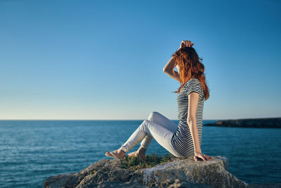 Man sitting on rock by sea against clear sky