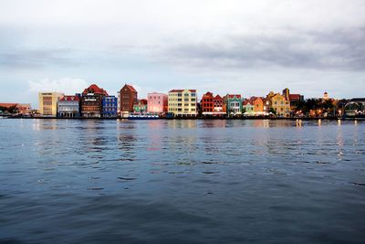 Buildings by river against sky in city