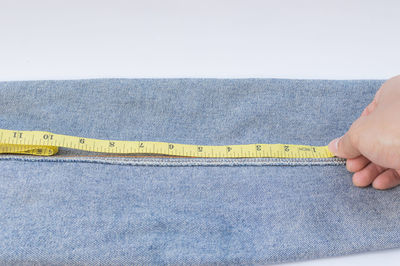 Close-up of person taking measurement of jeans over white background