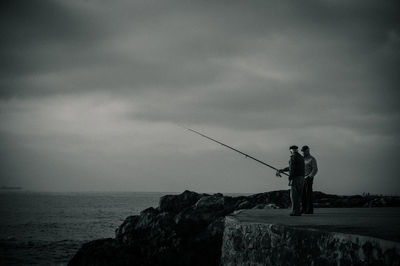 Man fishing at sea shore against sky