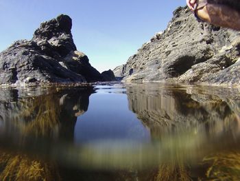 Close-up of hand on rock by lake against sky