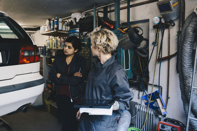 Female mechanic with customer examining car at auto repair shop