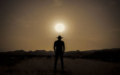 Rear view of man standing on field against sky during sunset