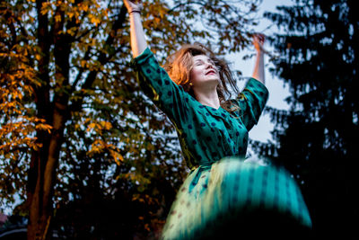 Low angle view of young woman jumping against trees during sunset