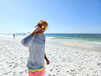 Young millennial on beach calling a friend on cellphone.