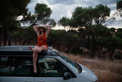 Woman sit down on the roof of a camper van in the forest at sunset