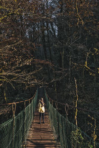 Rear view of woman walking on footbridge in forest