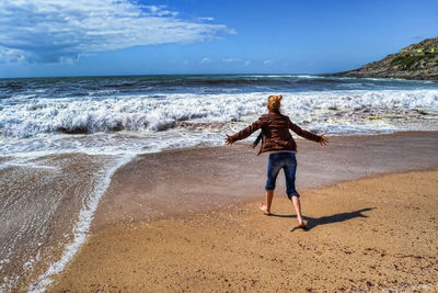 Rear view of woman on beach against sky