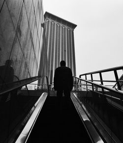 Rear view of man standing on escalator by building