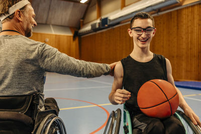 Male athlete with disability motivating girl sitting on wheelchair with basketball at sports court