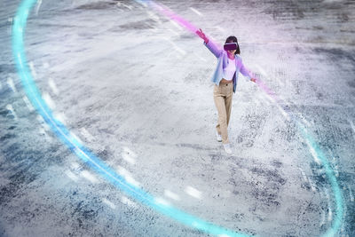 Teenage girl using virtual reality headset with arms outstretched making glowing circle on footpath