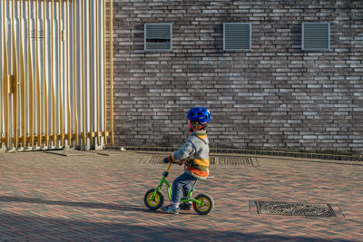 Full length of boy riding bicycle toy against brick wall